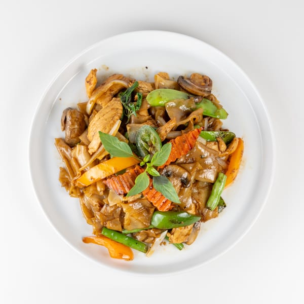 Pad See Ew with chicken, wide noodles, mushrooms, bell peppers, and basil on a white plate.
