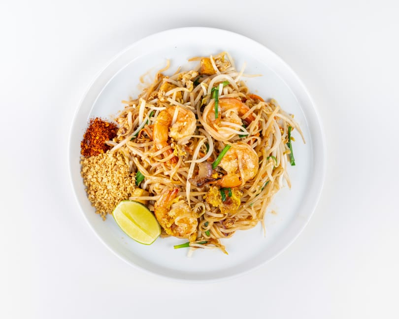 Pad Thai with shrimp, bean sprouts, and lime, served with crushed peanuts and chili flakes.