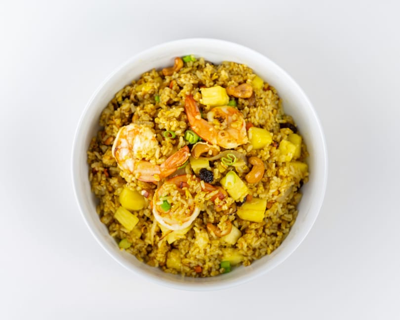 Golden pineapple fried rice with shrimp, cashews, and green onions in a white bowl.