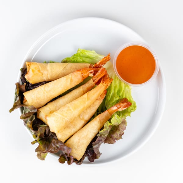 Shrimp spring rolls with tails exposed, served on lettuce with a side of orange dipping sauce.