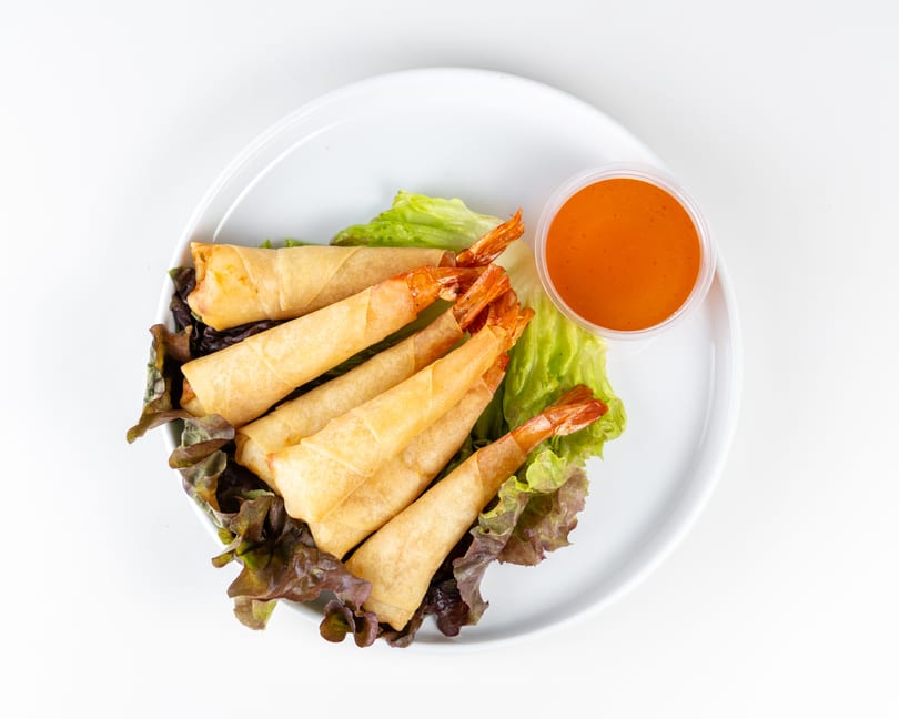 Shrimp spring rolls with tails exposed, served on lettuce with a side of orange dipping sauce.
