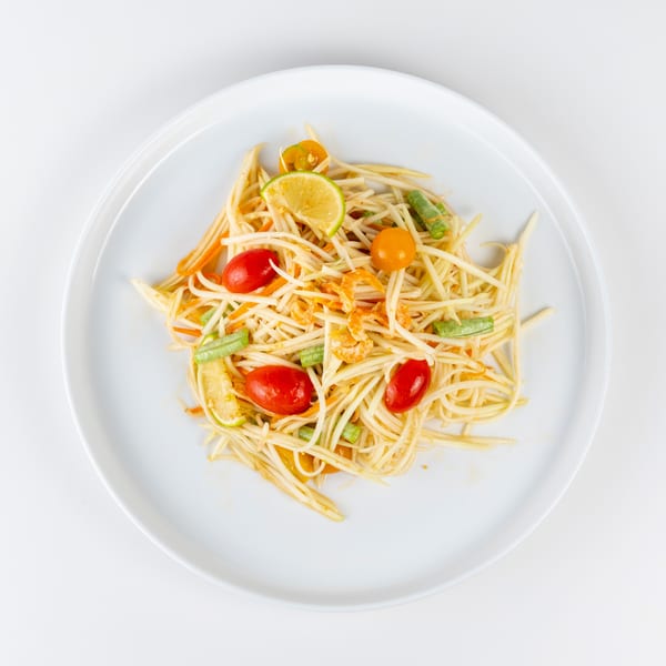 Som Tum, a Thai green papaya salad with tomatoes, green beans, and dried shrimp on a white plate.