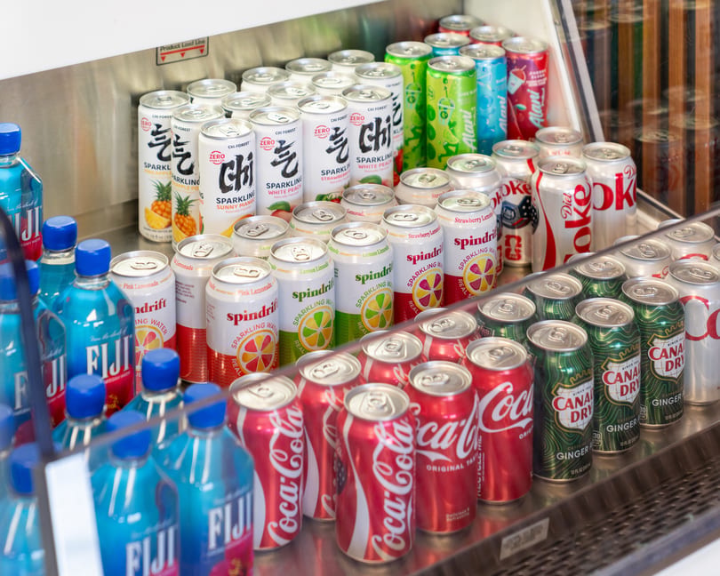 A refrigerated display case filled with various canned and bottled beverages, including Coca-Cola and Fiji water.