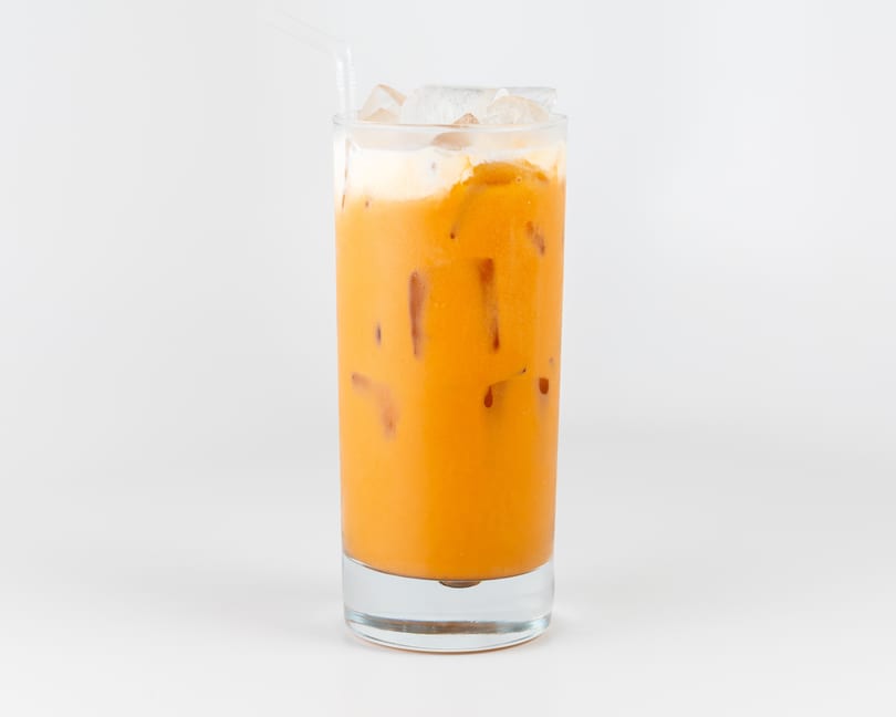 Iced Thai tea with a creamy top layer and ice cubes in a tall glass.