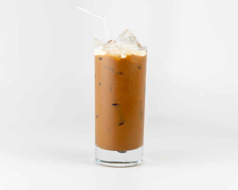 Iced coffee with cream and ice cubes in a tall glass with a straw on a white background.